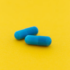 Pharmaceutical medicine blue capsule pills on a yellow background