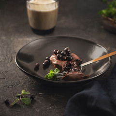 Chocolate muffin with blueberries in black plate on dark background with coffee