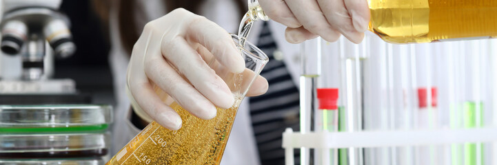 Female hand in white protective gloves pours beer from bottle in test tube closeup. Food test concept