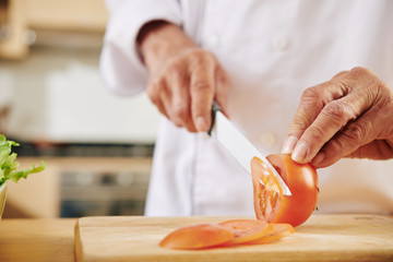 Close-up image of man cutting fresh tomato with sharp knife when cooking lunch at home
