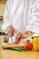 Professional chef in white jacket cutting red bell pepper for tasty healthy dish