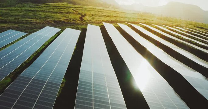 Aerial view flying over a solar panel farm at sunrise with verdant green mountains in the background, the future of green renewable energy is the sun