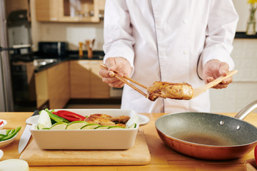 Chef using chopsticks when putting fried chicken tights from frying pan to baking tray