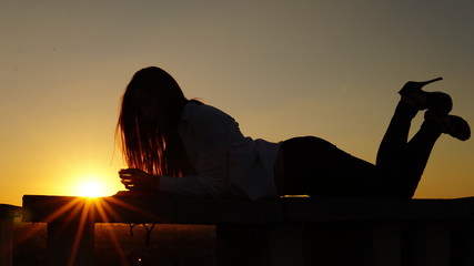 Young girl in sports uniform sits on the edge of the roof during sunset.