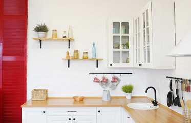 Modern new light interior of kitchen with white furniture, white brick wall and different cute jars on the shelves.