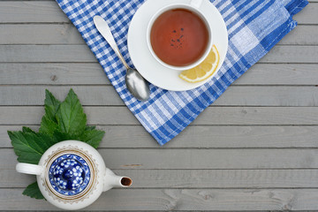 cup of black tea with lemon slice and tea pot on wooden table, top view