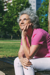 Dreamy old lady relaxing in city park. Pensive senior grey haired woman in casual sitting on bench outdoors, leaning chin on hand, thinking, looking up. Thinking in park concept