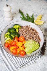 A bowl of vegan food, a vegan dinner of boiled buckwheat, colored tomatoes, avocado and broccoli. Top view, selective focus