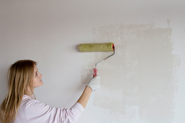 A woman enthusiastically and painstakingly paints a wall in white. Place for text