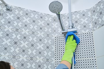 Woman cleaning and polishing shower, glass, faucet, tiled wall
