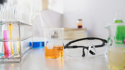 Photo of scientific experiment desk with chemistry glassware, stack of books, colored liquids and safety glasses putting on it. Concept of orderly workplace for the scientist.