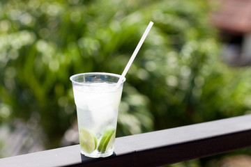A large glass of water, sliced lime and ice on the railing with a blurred background.