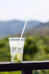 A large glass of water, sliced lime and ice on the railing with a blurred background.