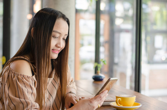 Charming woman with beautiful smile reading good news on mobile phone during rest in coffee shop, happy watching her photo on cell telephone while relaxing in cafe during free time