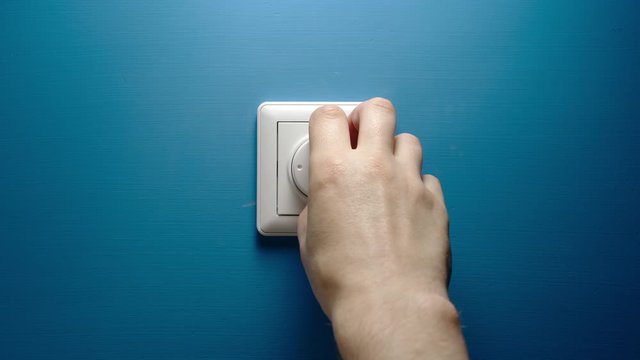 Male hand turns dimmer button on a blue wall