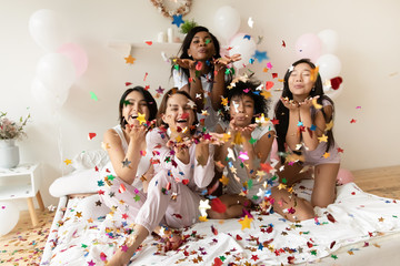 Portrait happy diverse girls blowing confetti at camera at party