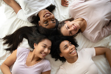 Fototapeta premium Top view happy girls friends lying on bed, having fun