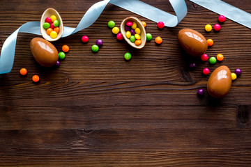 Easter background with chocolate eggs and dragees on dark wooden background top-down frame copy space