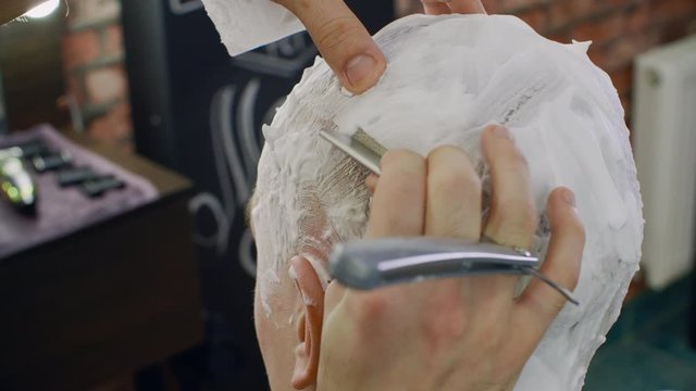 Barber hand shaving bald man with straight razor in male salon. Close up shaving head by straight razor and foam in barber shop. Male hair and head skin care