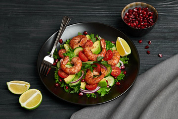 Shrimps salad with cherry tomatoes, cucumeber, avocado, lettuce and pomegranate on dish. Healthy seafood concept. Tasty grilled prawn shrimp and mix vegetable salad on black wood