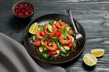 Shrimps salad with cherry tomatoes, cucumeber, avocado, lettuce and pomegranate on dish. Healthy seafood concept. Tasty grilled prawn shrimp and mix vegetable salad on black wood