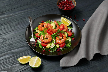Shrimps salad, avocado, lettuce, cherry tomatoes. Home made vegetarian shrimp salad. Seafood concept. Tasty veg mixed leaves, grilled prawn shrimps in plate on black wood background.