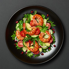 Shrimps salad with cherry tomatoes, cucumeber, avocado, lettuce and pomegranate on dish. Healthy seafood concept. Tasty grilled prawn shrimp and mix vegetable salad on black, closeup