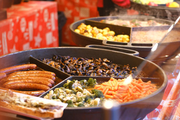 Cauliflower, mushrooms, carrots, sausages fry on a two big round pans in outdoor cafe