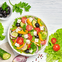 Greek salad with cucumeber, olives, feta cheese, cherry tomatoes, bell pepper, onion and lettuce. Diet, vitamin food. Healthy vegetarian meal concept. Tasty salad in bowl on white wood, top view.