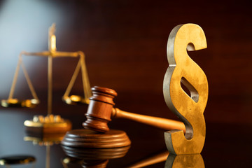 Law and justice concept. Judge’s gavel, scale and paragraph sign on the shining wooden brown table and the brown background.