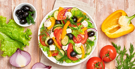 Greek salad with cucumeber, olives, feta cheese, cherry tomatoes, bell pepper, onion and lettuce. Diet, vitamin food. Healthy vegetarian meal concept. Tasty salad in bowl on wood, banner.