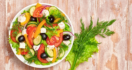 Greek salad with cucumeber, olives, feta cheese, cherry tomatoes, bell pepper, onion and lettuce. Diet, vitamin food. Healthy vegetarian meal concept. Tasty salad in bowl on wood, top view.