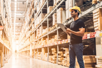 Smart Indian engineer man worker wearing safety helmet doing stocktaking of product management in...