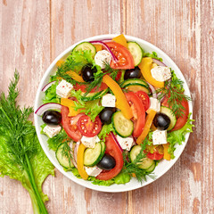 Greek salad with cucumeber, olives, feta cheese, cherry tomatoes, bell pepper, onion and lettuce. Diet, vitamin food. Healthy vegetarian meal concept. Tasty salad in bowl on wood, top view.