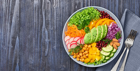 Buddha bowl salad with avocado, tomato, lettuce, cucumber, red cabbage, chickpeas, pomegranate. Paleo diet, healthy vegan and balanced food concept. Fresh rainbow mix green salad on wood. Copy space