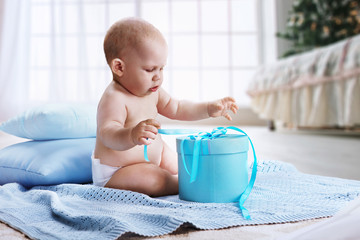Baby. Newborn in the diaper with the blue present in the hands sitting on the floor. 