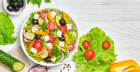 Greek salad with cucumeber, olives, feta cheese, cherry tomatoes, bell pepper, onion and lettuce. Diet, vitamin food. Healthy vegetarian meal concept. Tasty salad in bowl on white wood, top view.