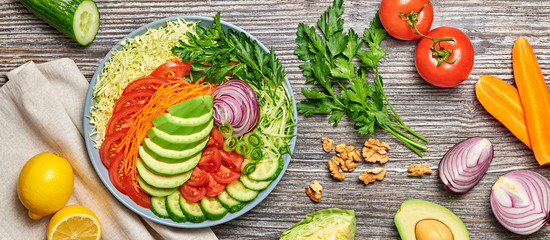 Fresh salad with avocado, lettuce, cucumber, cabbage, carrot, onion. Diet, healthy vegan salad, balanced food concept. Buddha bowl mix vegetable homemade salad on wood, flat lay. Banner