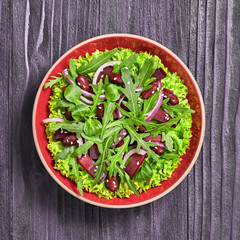 Vegan beetroot salad with red bean, lettuce, arugula, sunflower, sesame seed. Home made vegetarian beet max leaves salad on wood background. Tasty fresh beetroot diet vegan dish. Top view.