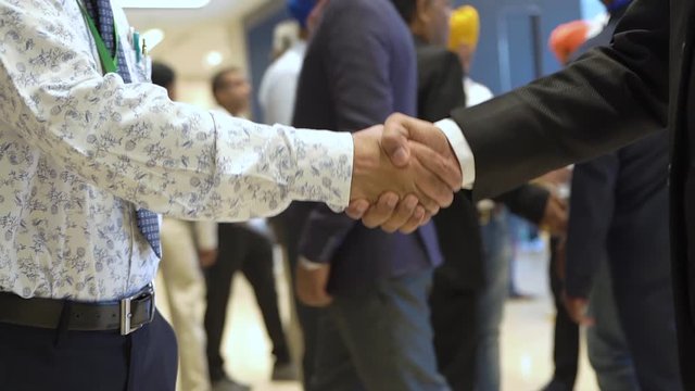 Two business, business men shake hands at a major conference, seminar, meeting, meeting. In the background a lot of people, everyone communicates