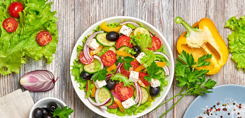 Greek salad with cucumeber, olives, feta cheese, cherry tomatoes, bell pepper, onion and lettuce. Diet, vitamin food. Healthy vegetarian meal concept. Tasty salad in bowl on wood, flat lay.