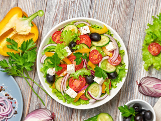 Greek salad with cucumeber, olives, feta cheese, cherry tomatoes, bell pepper, onion and lettuce. Diet, vitamin food. Healthy vegetarian meal concept. Tasty salad in bowl on wood, flat lay.