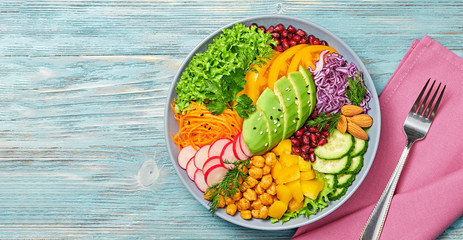 Buddha bowl salad with avocado, tomato, lettuce, cucumber, red cabbage, chickpeas, pomegranate. Paleo diet, healthy vegan and balanced food concept. Fresh rainbow mix green salad on blue wood