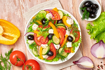 Greek salad with cucumeber, olives, feta cheese, cherry tomatoes, bell pepper, onion and lettuce. Diet, vitamin food. Healthy vegetarian meal concept. Tasty salad in bowl on wood, top view.