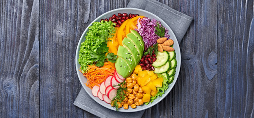 Buddha bowl salad with avocado, tomato, lettuce, cucumber, red cabbage, chickpeas, pomegranate. Paleo diet, healthy vegan and balanced food concept. Fresh rainbow mix green salad on wood, top view.