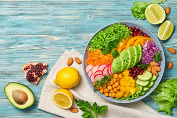 Buddha bowl salad with avocado, tomato, lettuce, cucumber, red cabbage, chickpeas, pomegranate. Paleo diet, healthy vegan and balanced food concept. Fresh rainbow mix green salad on blue wood