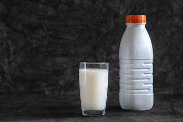 A glass with milk and a plastic white milk bottle on a black background. Space for text, minimalism. Liquid in a plastic container.