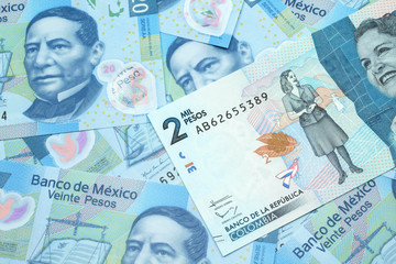 A close up image of a blue two thousand Colombian peso bank note on a background of Mexican twenty peso bank notes in macro