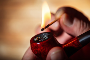 The man gets a light a pipe from a match. Close up. Selective focus.