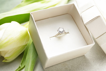 Box with beautiful engagement ring and tulip on light background